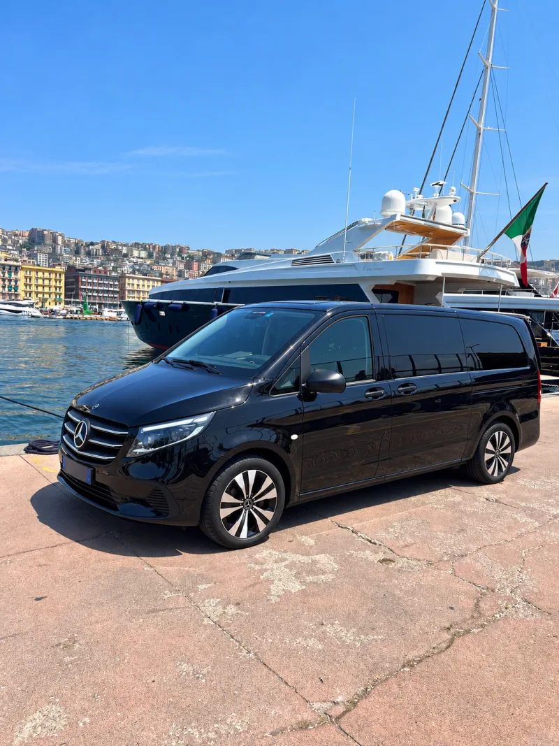 Der schwarze Mercedes Vito Extralong 2026 am Kai des Hafens von Neapel, mit einer Jacht und der Stadt im Hintergrund